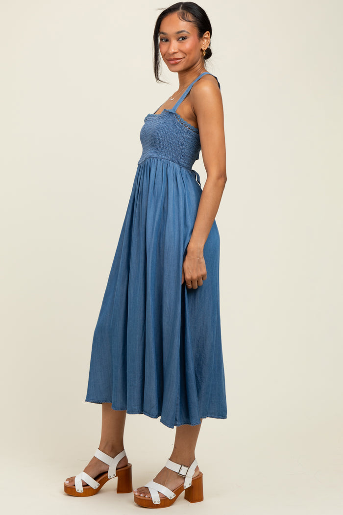 woman wearing a denim blue midi dress with smocked bodice and spaghetti straps, paired with white block heel sandals