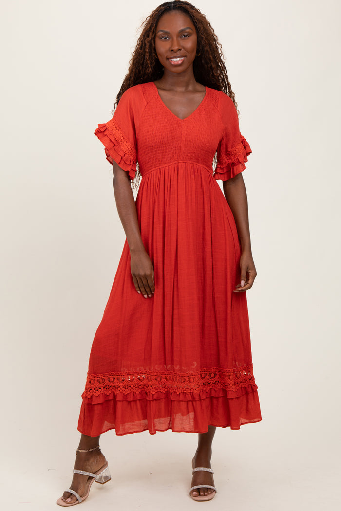 woman wearing a coral midi dress with ruffled sleeves and lace detailing, standing against a neutral background