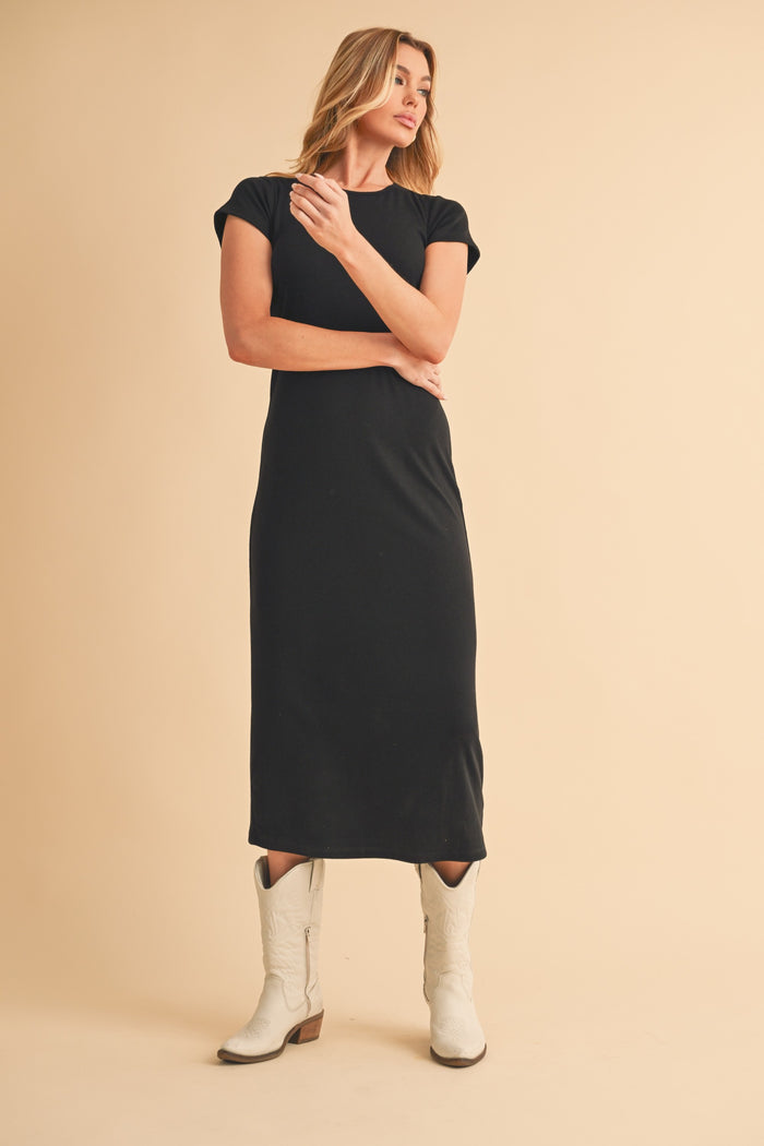 woman wearing a black cap sleeve midi dress and white cowboy boots, posing against a neutral background