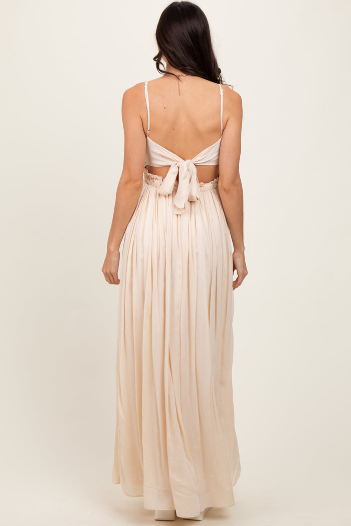 woman wearing a backless light beige maxi dress with a tied bow detail and pleated skirt