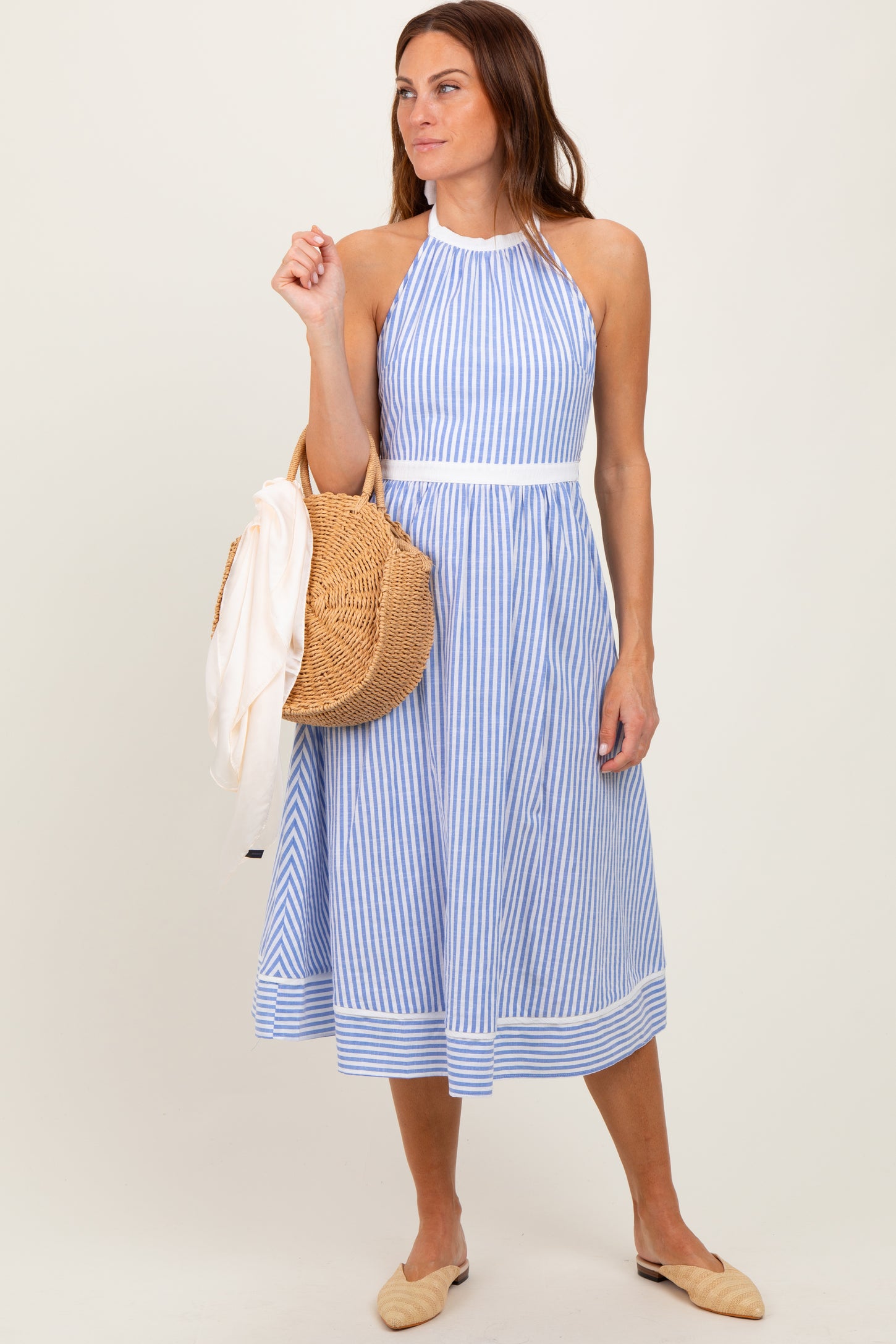 woman wearing a blue and white striped halter neck sundress and holding a straw bag