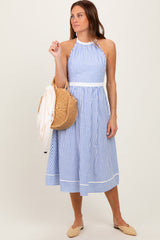 woman wearing a blue and white striped halter neck sundress and holding a straw bag