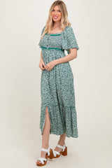 woman wearing a green floral maxi dress with short sleeves and a side slit, standing and smiling