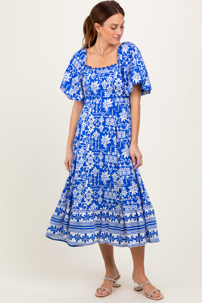 woman wearing a blue floral print midi dress with puff sleeves and a square neckline, standing on a light background