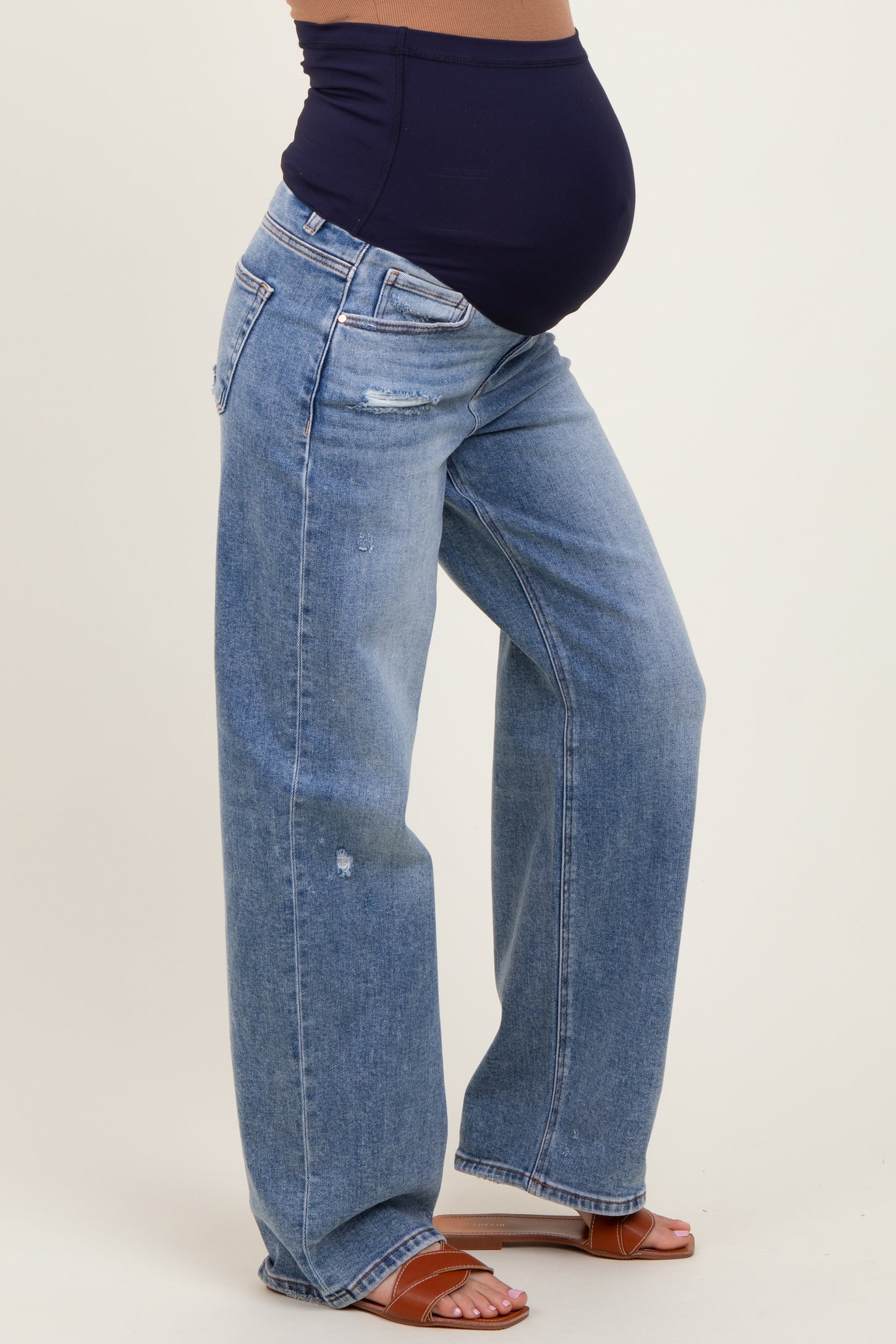 woman wearing light blue distressed maternity jeans with a black belly band and showing her baby bump