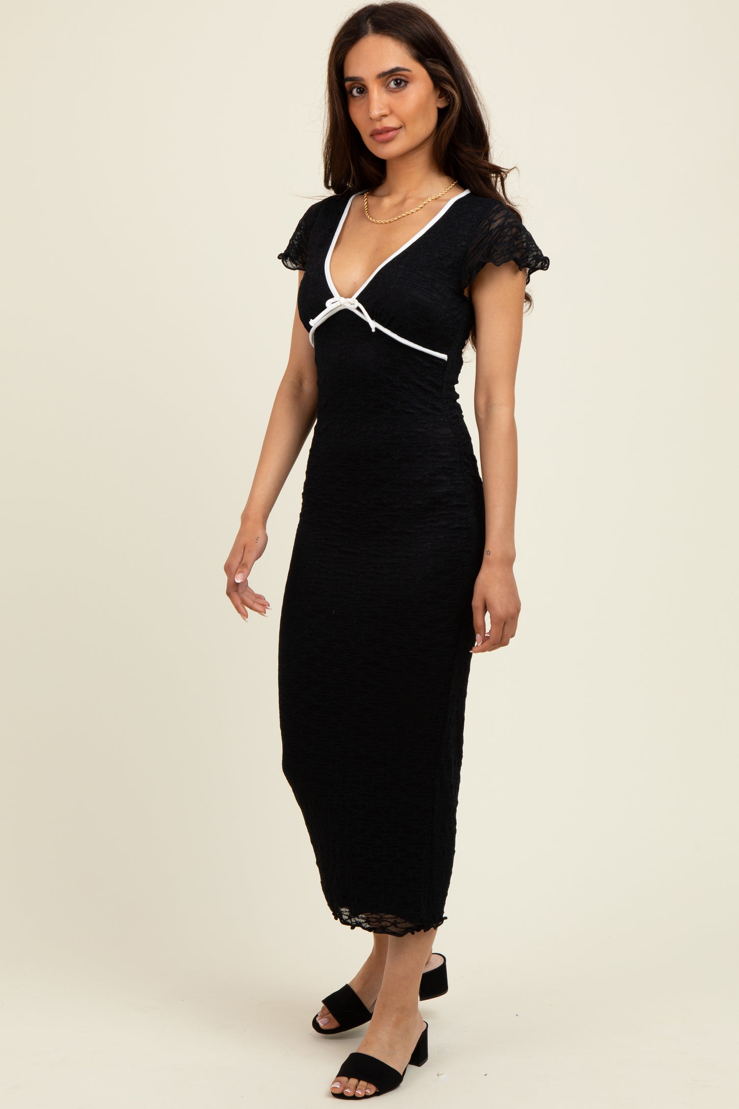 woman wearing a black midi dress with cap sleeves and a white ribbon detail, standing against a light background