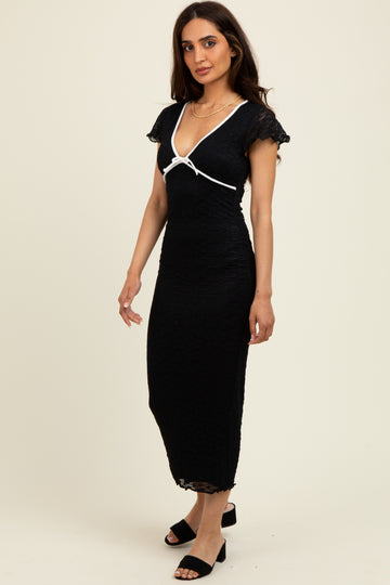woman wearing a black midi dress with cap sleeves and a white ribbon detail, standing against a light background