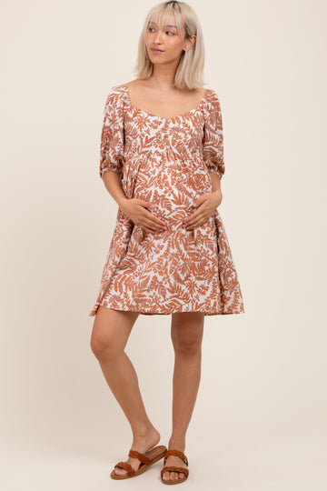 woman wearing a brown and white floral print maternity dress, gently cradling her baby bump