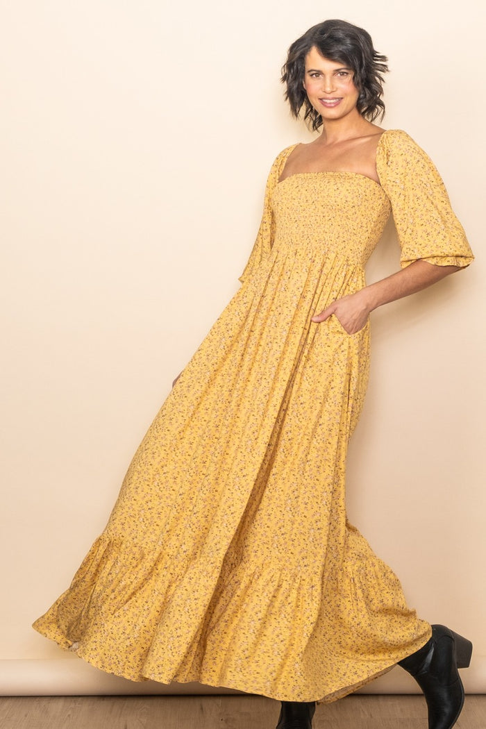 woman wearing a yellow floral maxi dress with a square neckline and short bell sleeves, posing confidently
