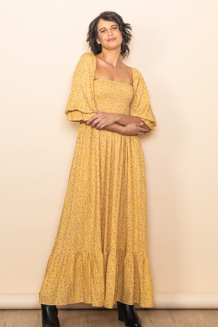 woman wearing a yellow floral maxi dress with puff sleeves and a tiered skirt