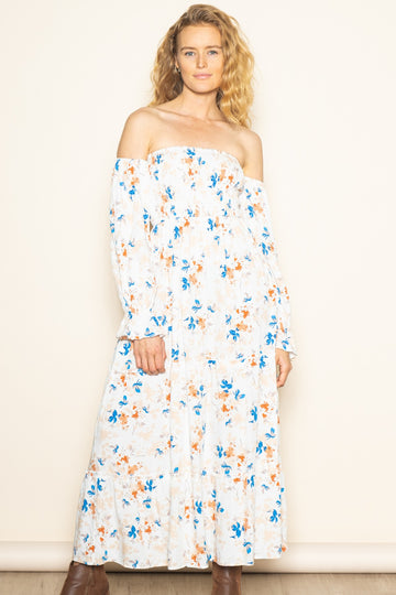 woman wearing a white off-the-shoulder floral maxi dress with blue and orange patterns and long sleeves