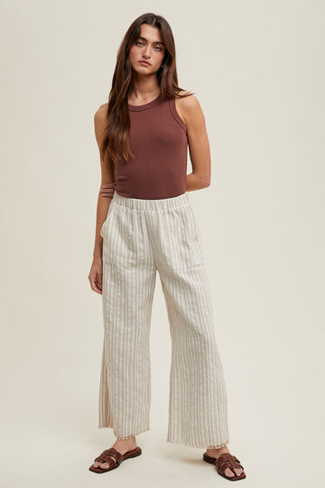 woman wearing a brown sleeveless bodysuit and cream striped wide-leg pants, standing against a neutral background