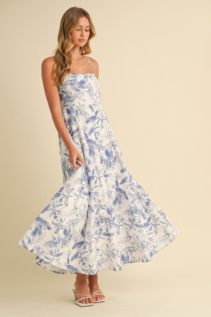 woman wearing a white floral maxi dress with blue print and spaghetti straps, twirling in the dress