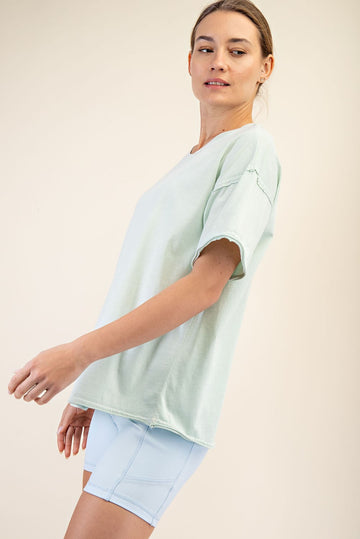 woman wearing a mint green oversized t-shirt and light blue athletic shorts, standing sideways with a relaxed expression