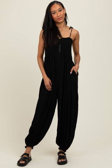 woman wearing a black sleeveless jumpsuit with a buttoned bodice and side pockets, styled with black sandals