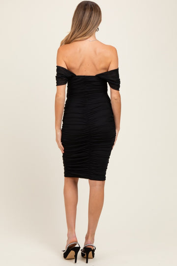 woman wearing a black off-the-shoulder maternity dress with ruching details, showing her back and fitted silhouette