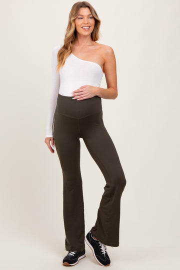 woman wearing a white one-shoulder top and olive green maternity flared leggings, smiling, with a baby bump visible