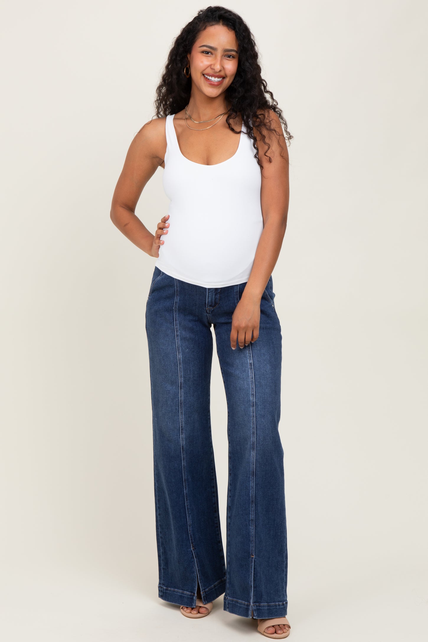 woman wearing a white maternity tank top and wide-leg denim jeans, showing her baby bump
