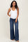 woman wearing a white maternity tank top and wide-leg denim jeans, showing her baby bump
