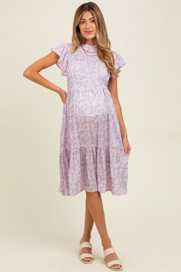 woman wearing a lilac floral maternity dress with ruffle sleeves and a tiered skirt, showing her baby bump