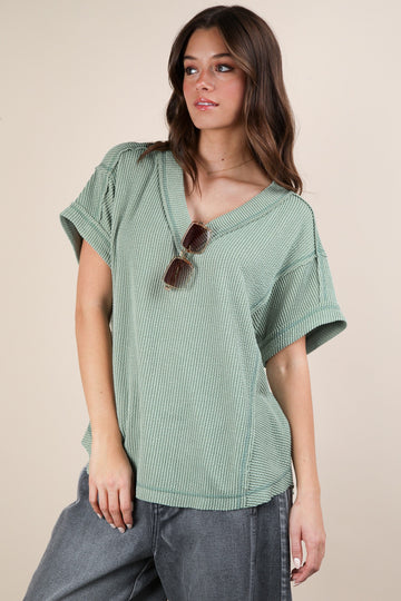 woman wearing a green short sleeve v-neck top with textured fabric and relaxed fit, paired with gray high-waisted pants