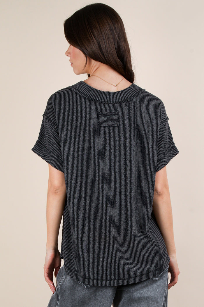 woman wearing a dark gray oversized short sleeve top with a textured knit design, showing the back view