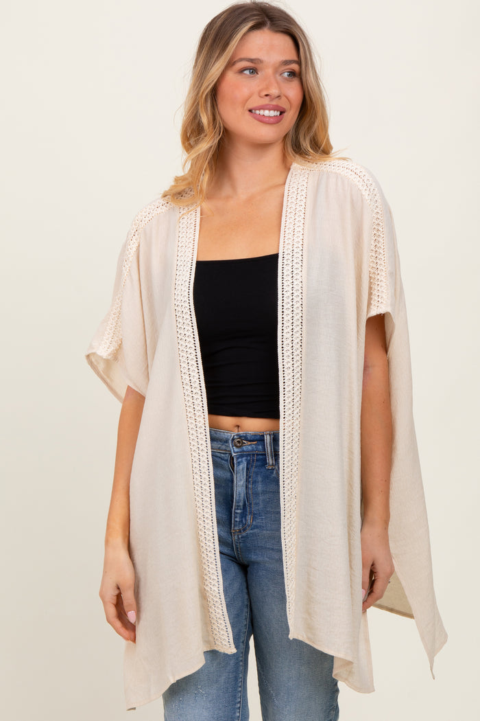 woman wearing a beige open-front kimono cardigan with lace details over a black crop top and blue jeans