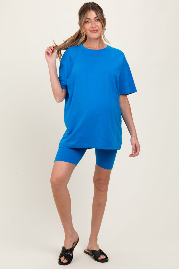 woman wearing a bright blue maternity oversized t-shirt and matching blue bike shorts, holding her hair up with one hand