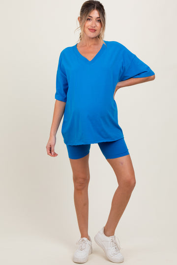 woman wearing a bright blue oversized maternity top and matching bike shorts, showcasing her baby bump