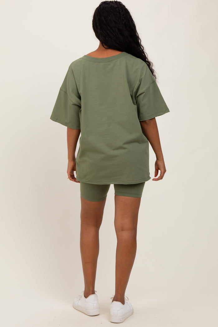 woman wearing an oversized olive green t-shirt and matching bike shorts, standing with her back to the camera