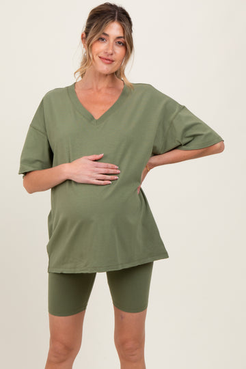 woman wearing a green oversized v-neck maternity t-shirt and matching bike shorts, holding her baby bump
