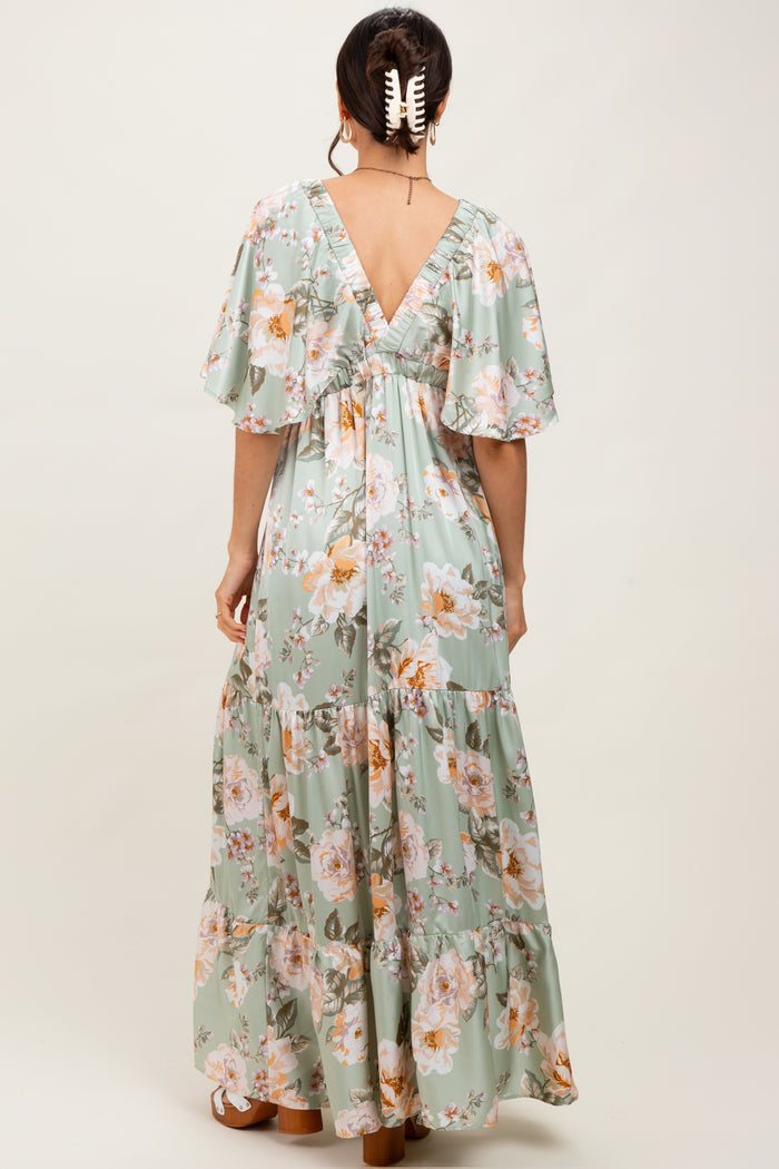 woman wearing a light green floral maxi dress with flutter sleeves and a v-back design