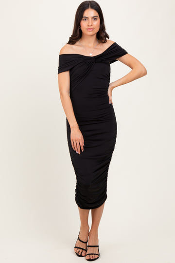 woman wearing a black off-the-shoulder bodycon dress with ruching details and strappy heels