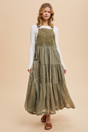 woman wearing a long olive green tiered maxi dress with embroidered flowers and adjustable straps
