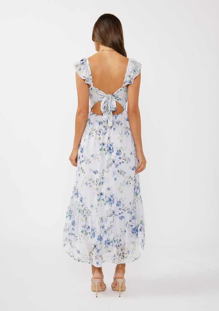 woman wearing a floral maxi dress with ruffled sleeves and a tie-back detail, showing skin at the back