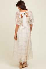 woman wearing a white lace midi dress with puff sleeves and a back bow detail, standing against a neutral background