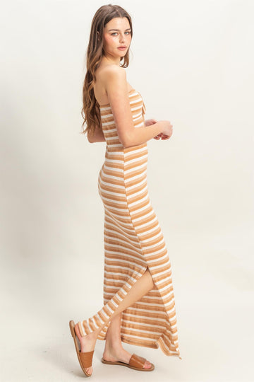 woman wearing a striped strapless maxi dress in tan and cream with a side slit, styled with brown sandals