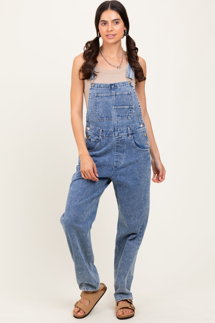 woman wearing a light beige tank top and blue denim overalls with side pockets and a relaxed fit