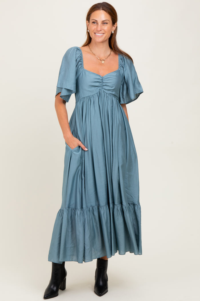 woman wearing a teal maxi dress with short puff sleeves and a tiered skirt, standing with hands in pockets