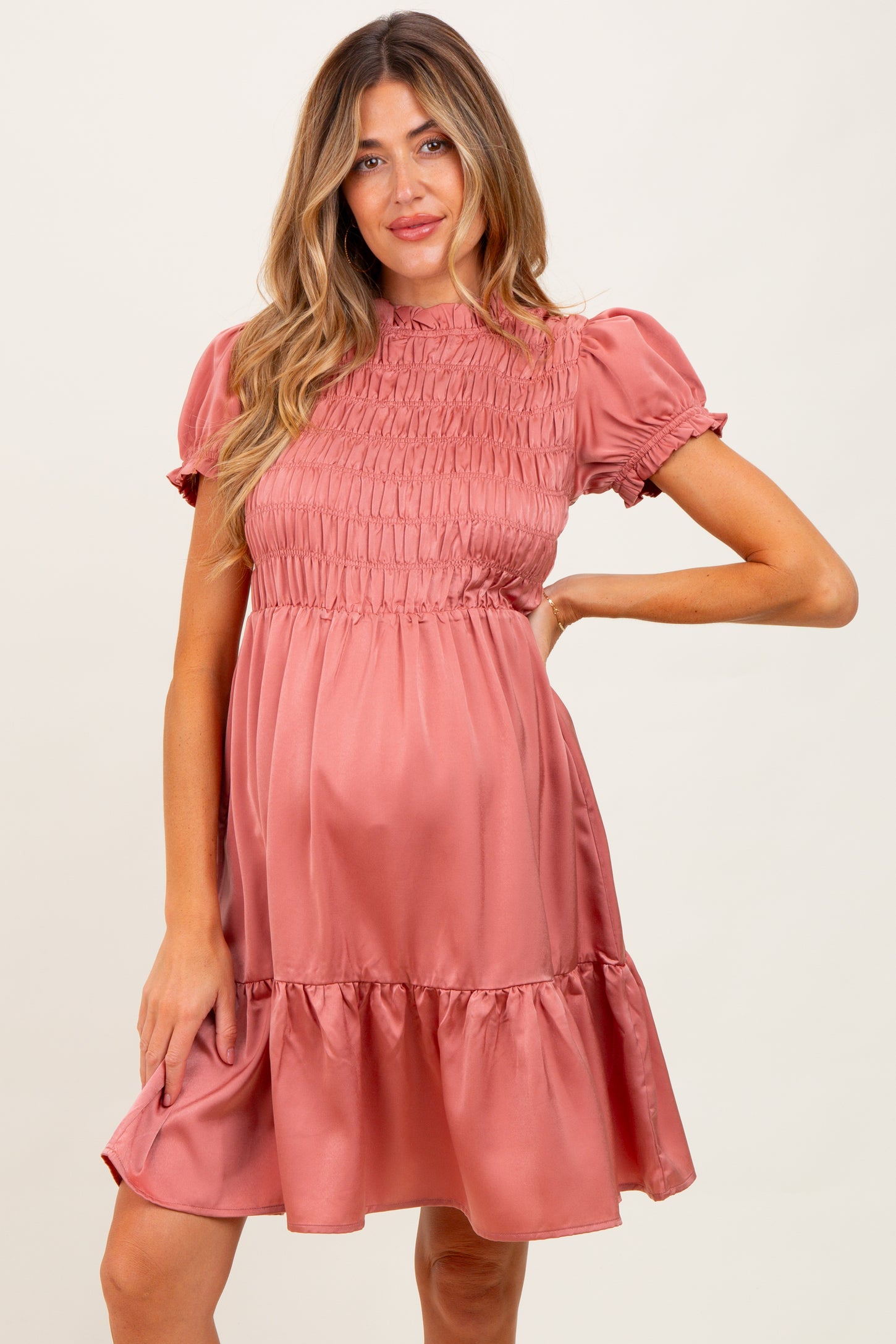 woman wearing a pink short sleeve maternity dress with smocked bodice and ruffled hem, showing her baby bump