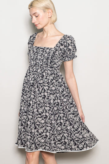 woman wearing a black floral print puff sleeve dress with a square neckline and flared skirt