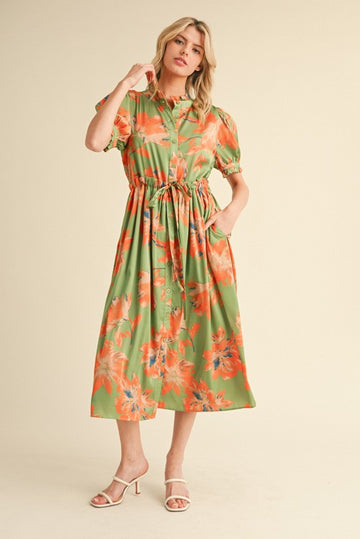 woman wearing a green floral midi dress with puff sleeves and a cinched waist, standing and posing with one hand in a pocket