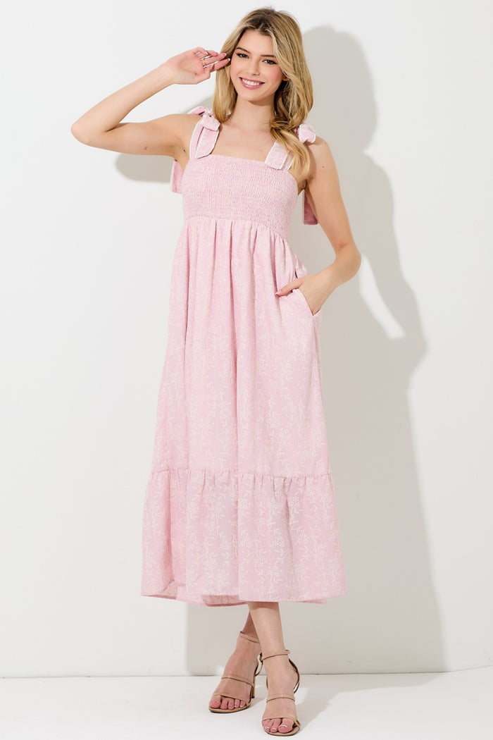 woman wearing a pink floral print maxi dress with smocked bodice and tie straps, featuring pockets and a tiered skirt