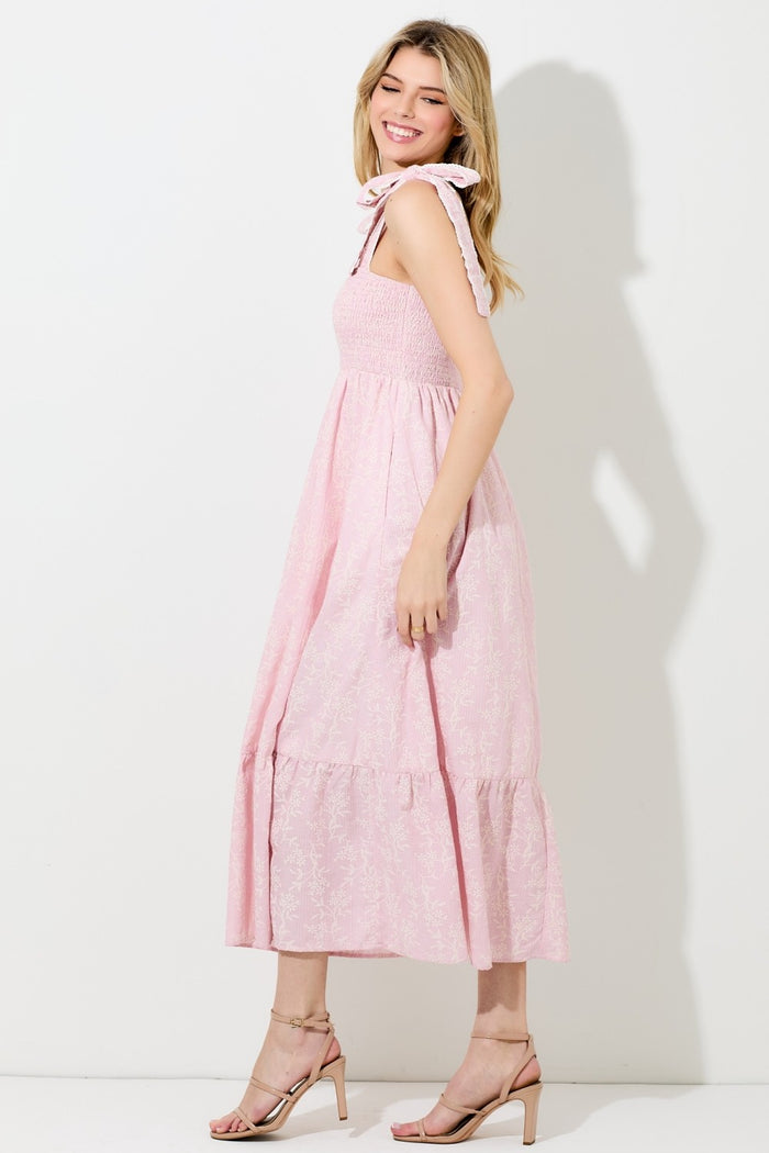 woman wearing a light pink floral midi dress with smocked bodice and bow detail on straps