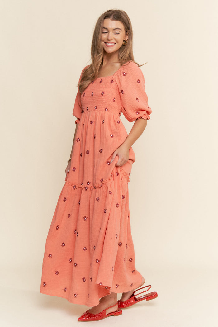 woman wearing a coral maxi dress with floral embroidery and puff sleeves, styled with red heeled sandals