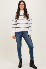 woman wearing a white and black striped sweater with a high neckline and long sleeves, paired with blue skinny jeans