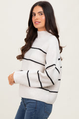 woman wearing a cream striped sweater with black lines and jeans, posing sideways with a slight smile