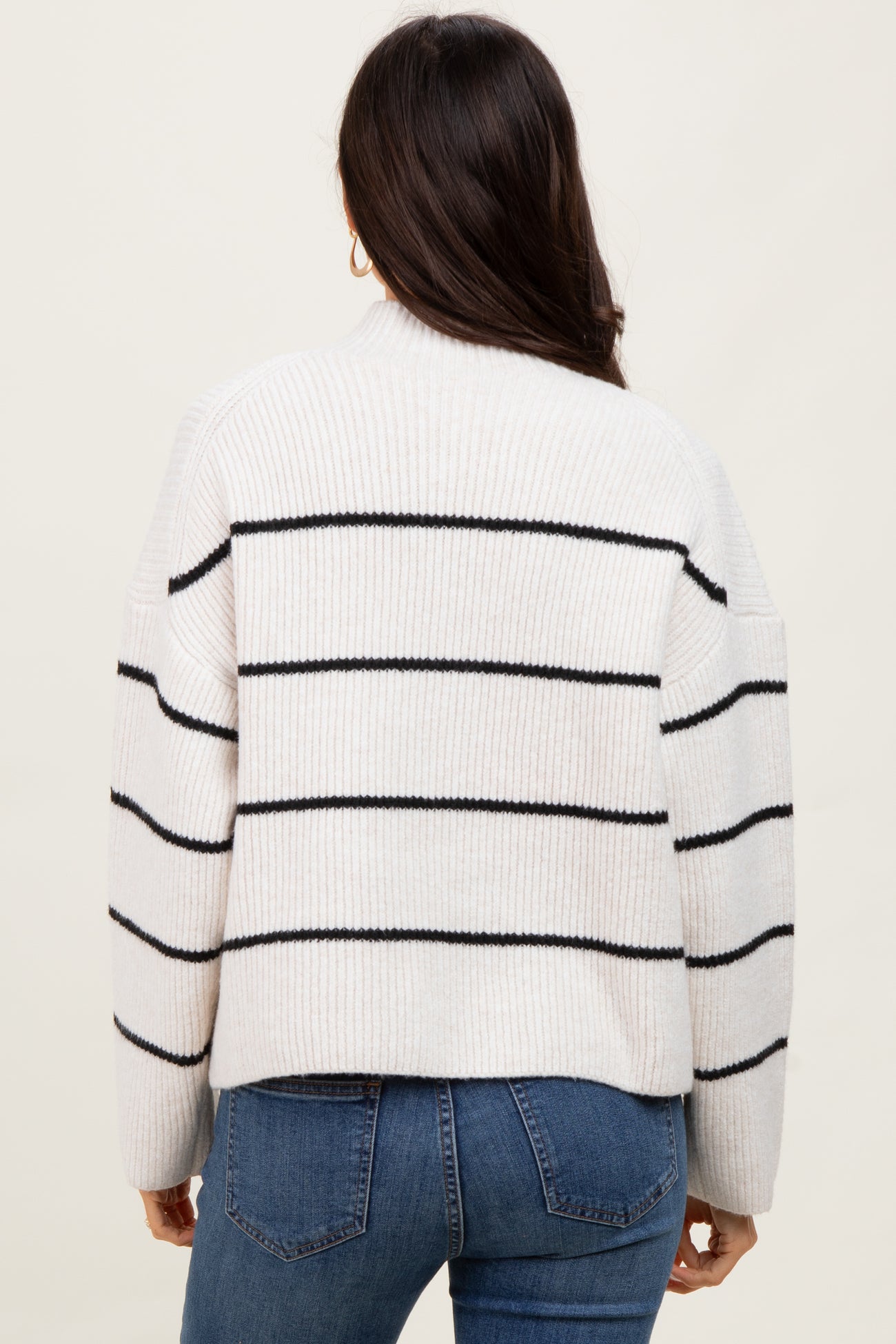 woman wearing a cream striped oversized sweater with black stripes, paired with blue jeans, view from the back
