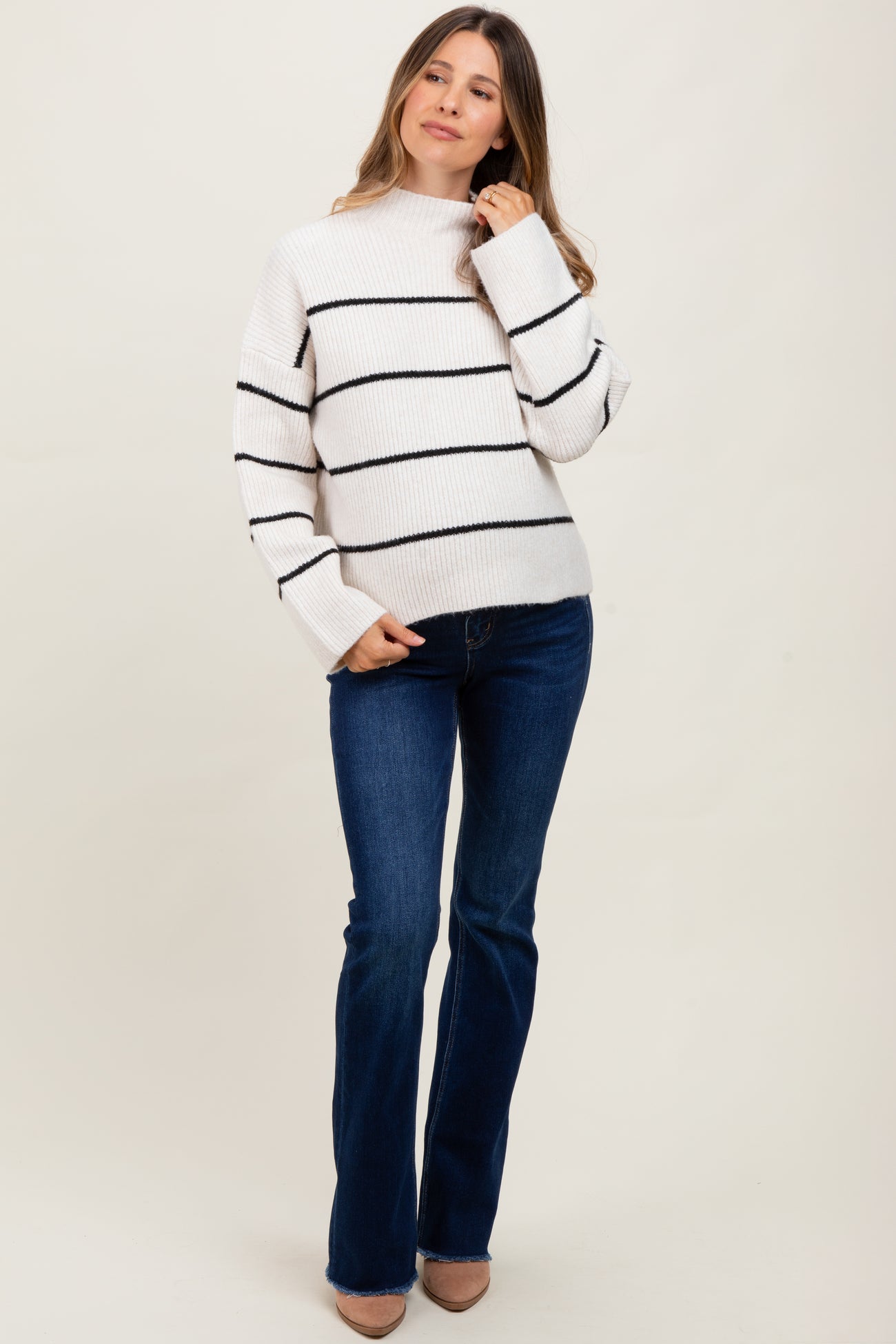 woman wearing a striped maternity sweater with a mock neck and flared jeans, looking stylish and comfortable