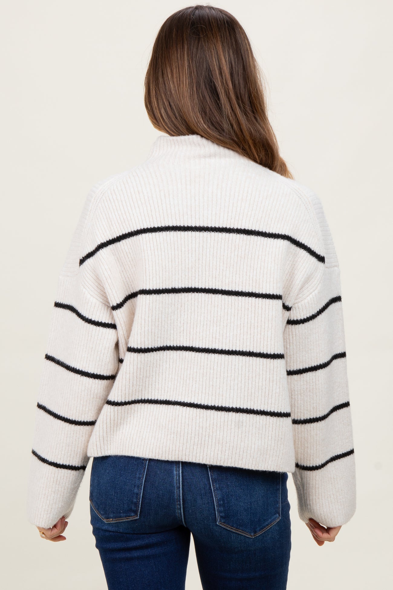 woman wearing a striped cream maternity sweater with black lines and paired with dark jeans, showing a relaxed fit from the back